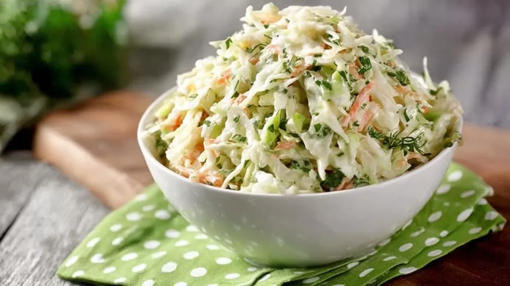 Creamy cilantro lime coleslaw in a white bowl with fresh cilantro and lime wedges